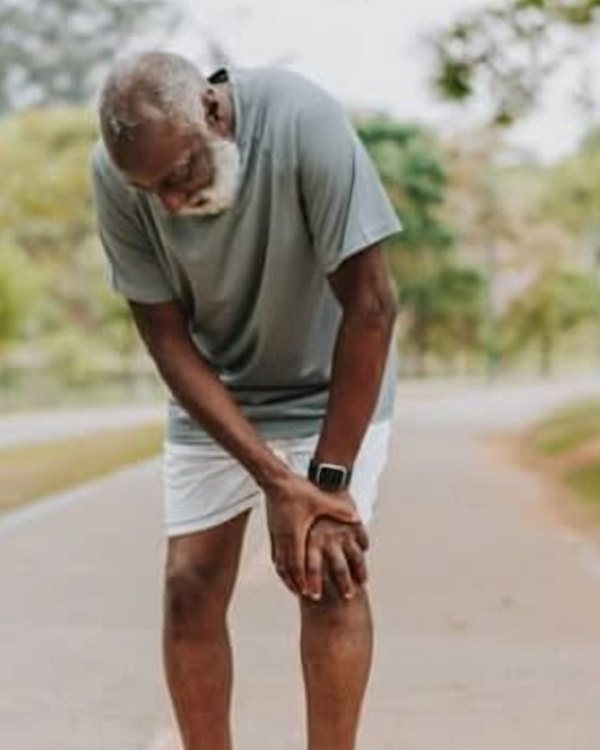 Older man pausing on a path with his hand on his knee, representing elderly mobility care