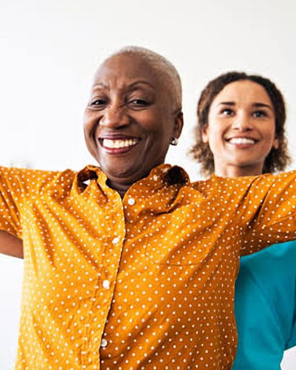 Older woman raising hand weights with a helper behind her, representing stroke rehabilitation